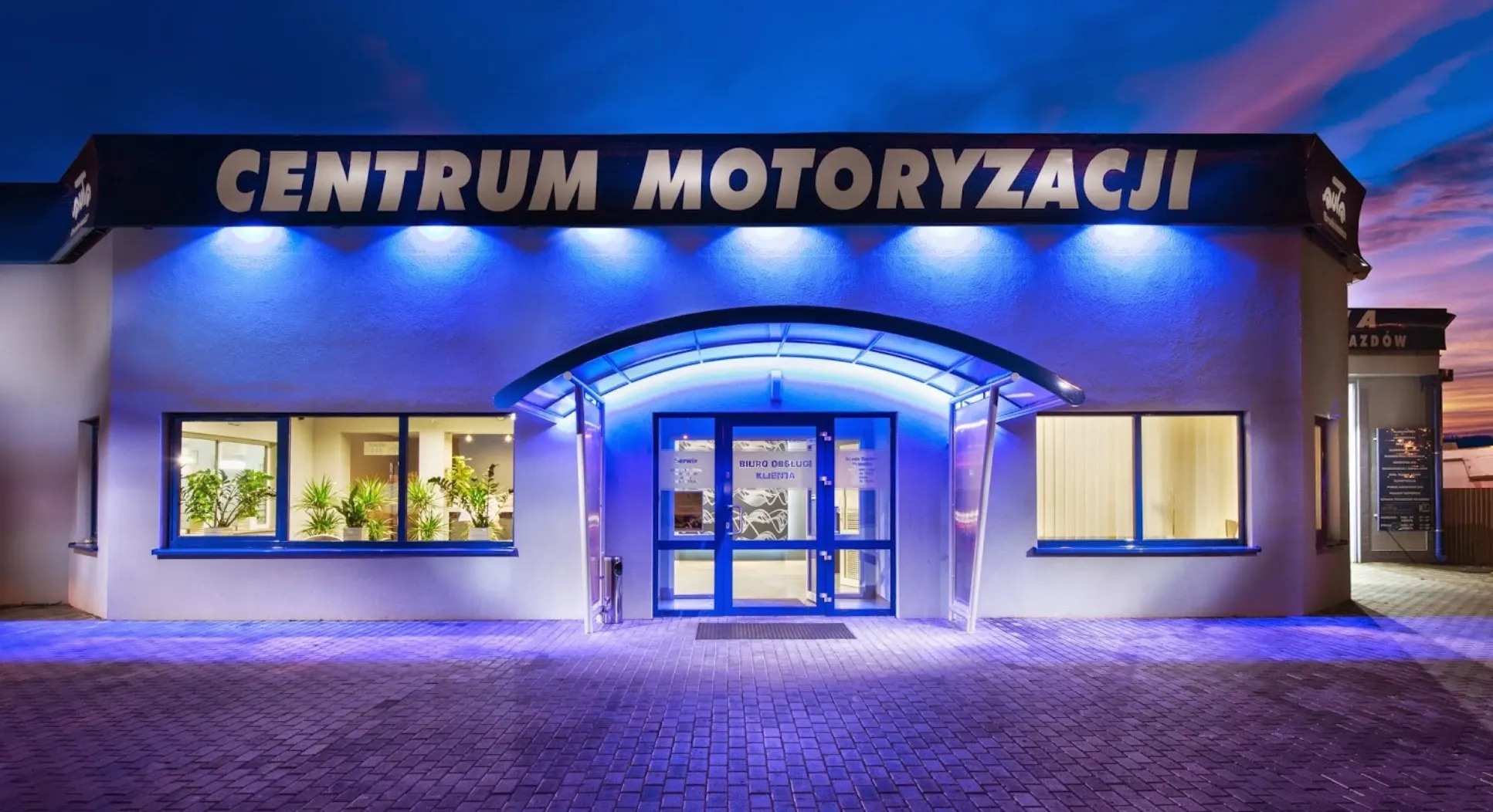 Podświetlone wejście do centrum motoryzacji Auto Brudniewicz wieczorem